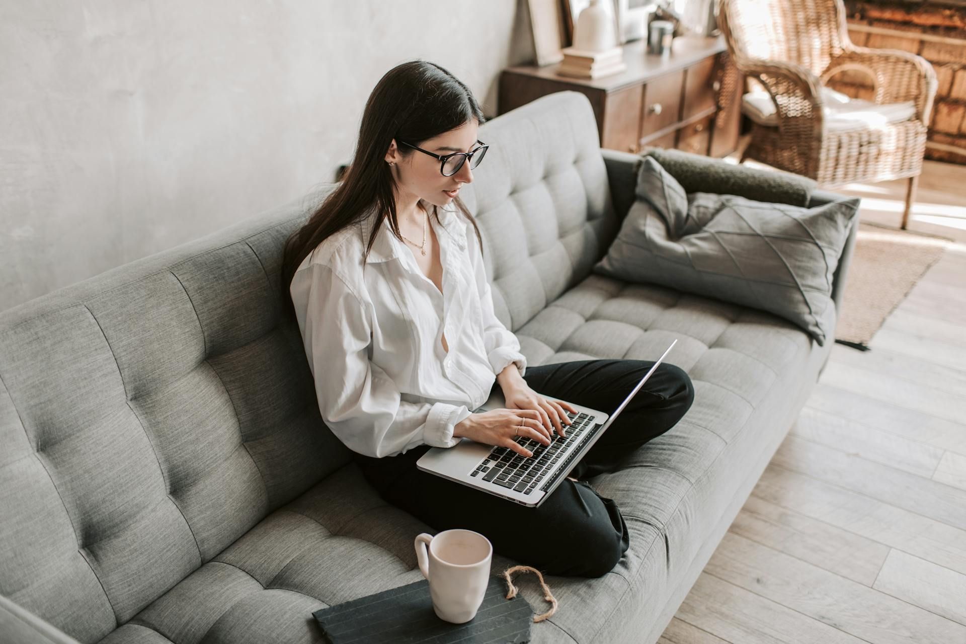 Eine Frau sitzt auf einem Sofa und schreibt auf einem Notebook eine E-Mail